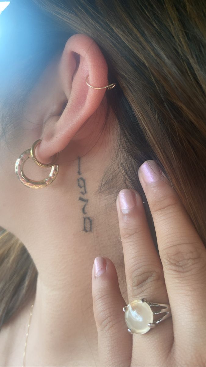 a woman with tattoos on her neck and behind the ear is a small pearl ring