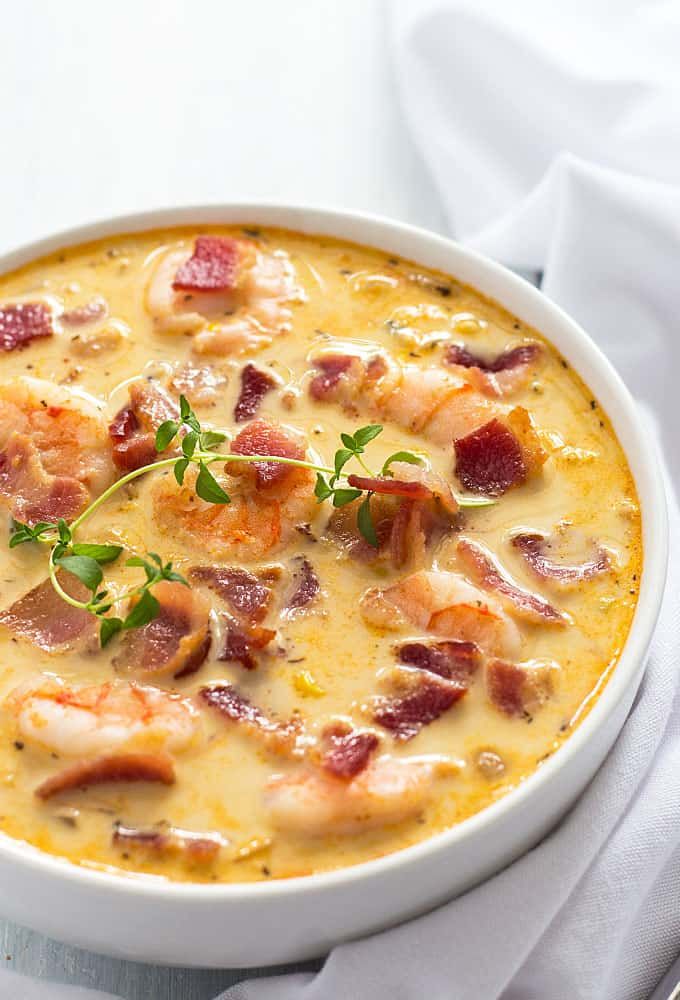 a close up of a bowl of soup with shrimp and bacon in it on a table