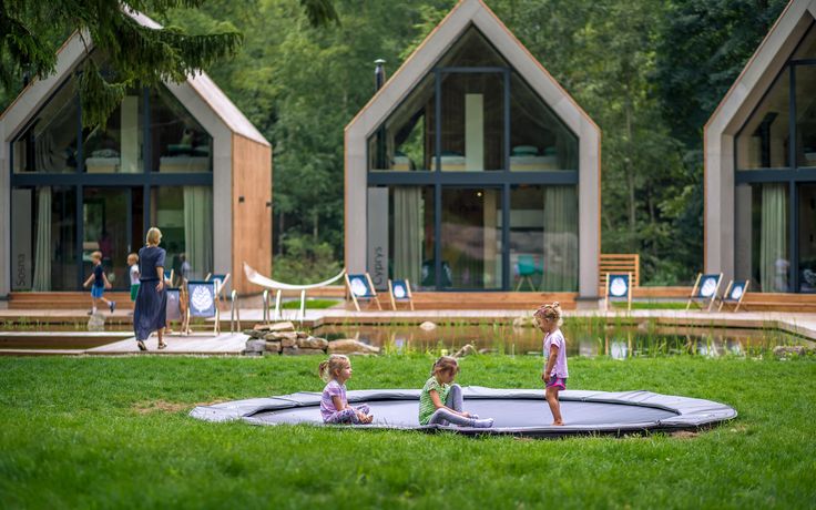 three children are playing on a trampoline in the grass near some houses and trees