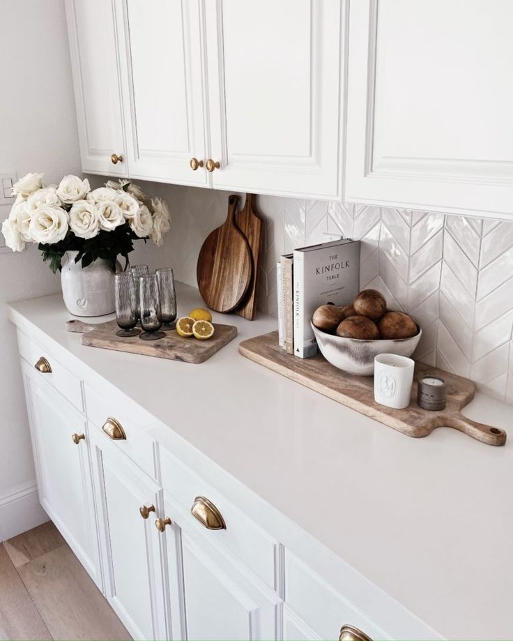 a kitchen counter with white cabinets and wooden cutting boards on it, along with flowers in vases