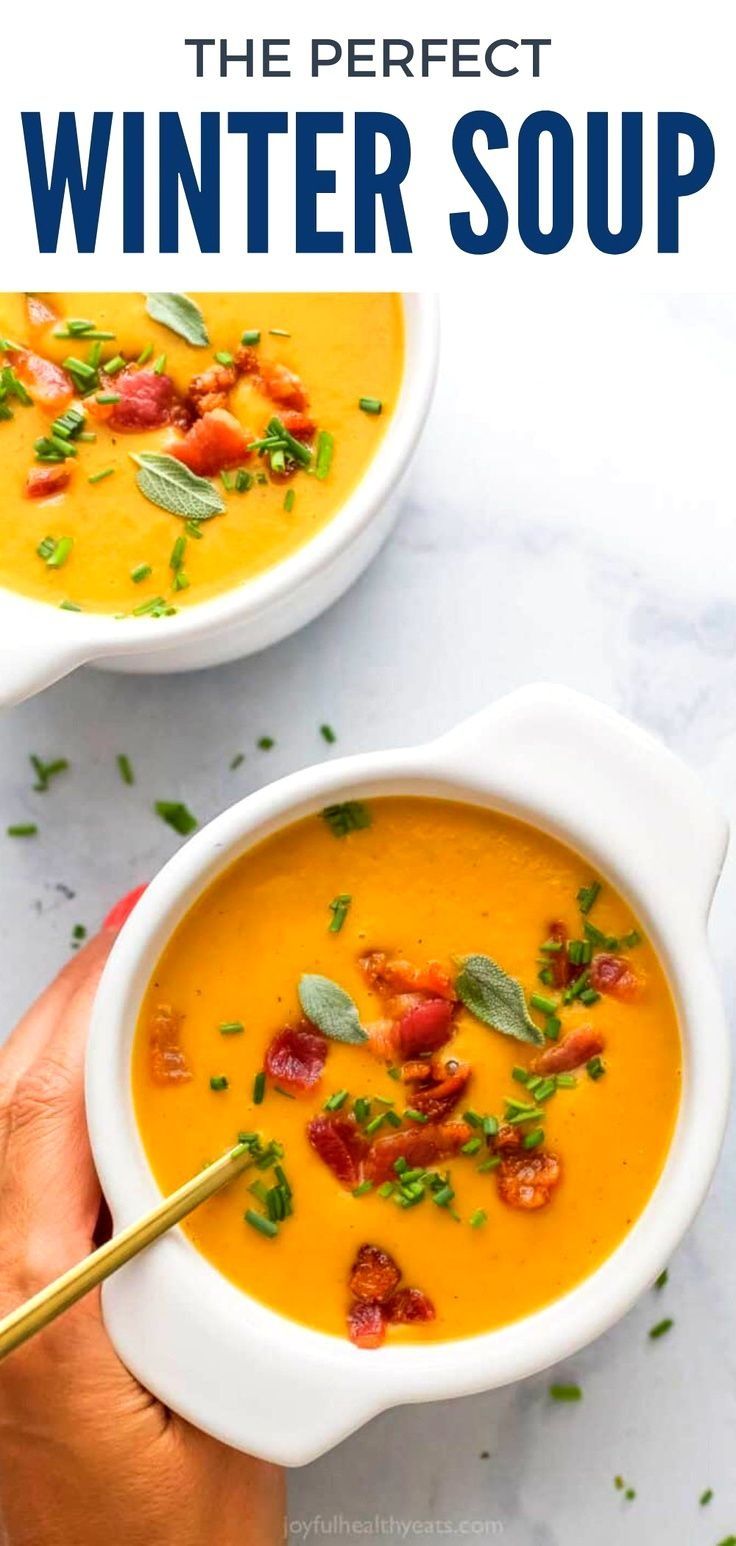 two white bowls filled with carrot soup and topped with bacon, parsley and basil