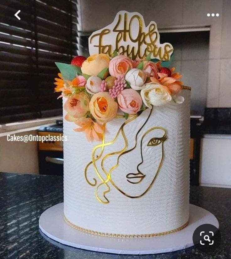 a white cake decorated with flowers and gold lettering