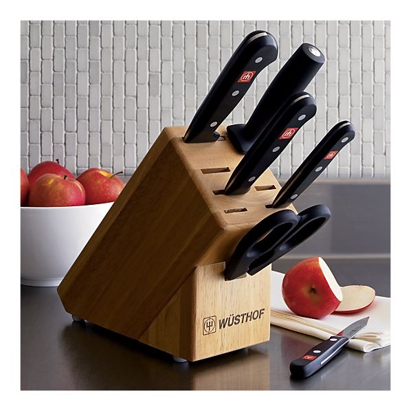 a wooden block holding knives and apples on a table