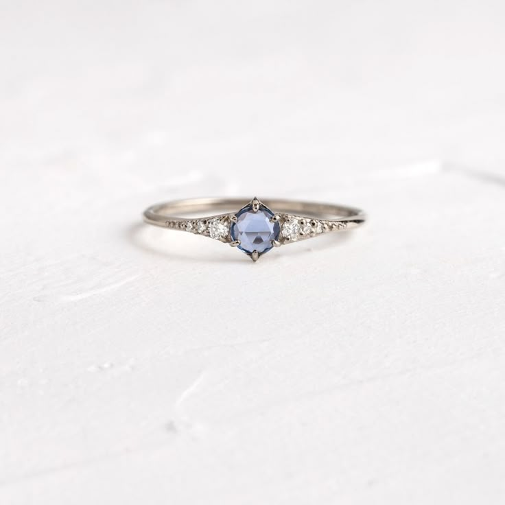 a white gold ring with an oval blue sapphire and diamond accents on the band, sitting on a plain surface