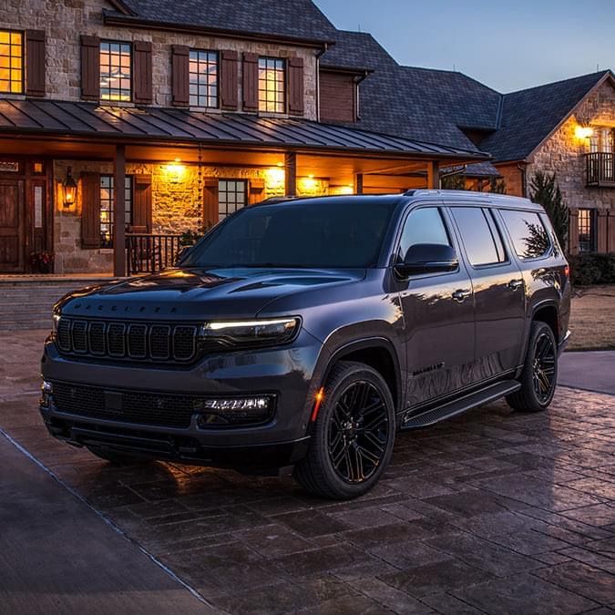 a black jeep parked in front of a large house at night with the lights on