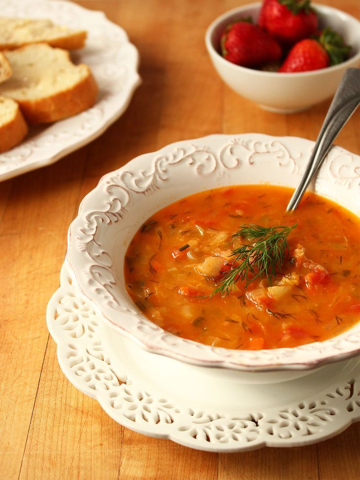 a bowl of soup with bread and strawberries in the background on a wooden table