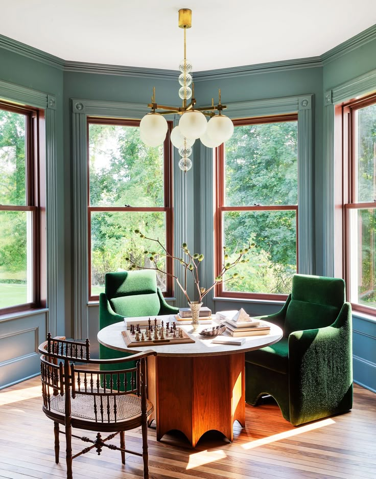 a dining room with green chairs and a round table in front of two large windows