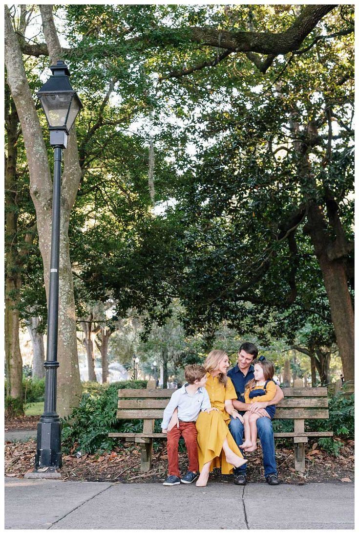 a family sitting on a park bench in front of a lamp post and tree lined street