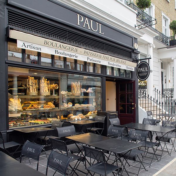 the outside of a bakery with tables and chairs in front of it, along side a sidewalk