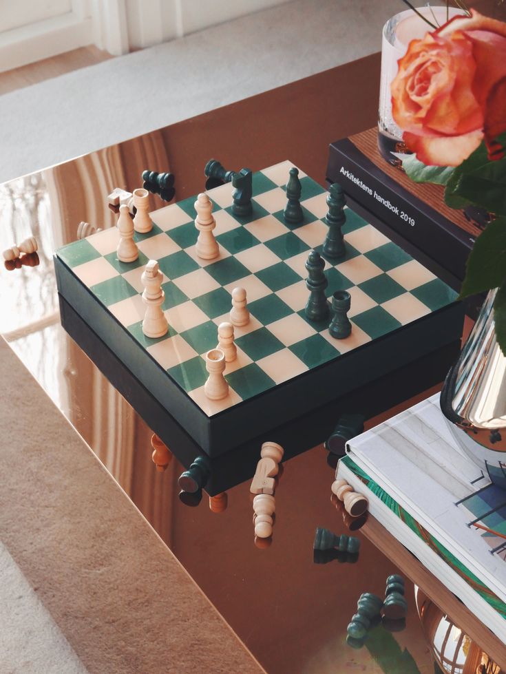 a chess board on a coffee table next to a vase with flowers and books in it