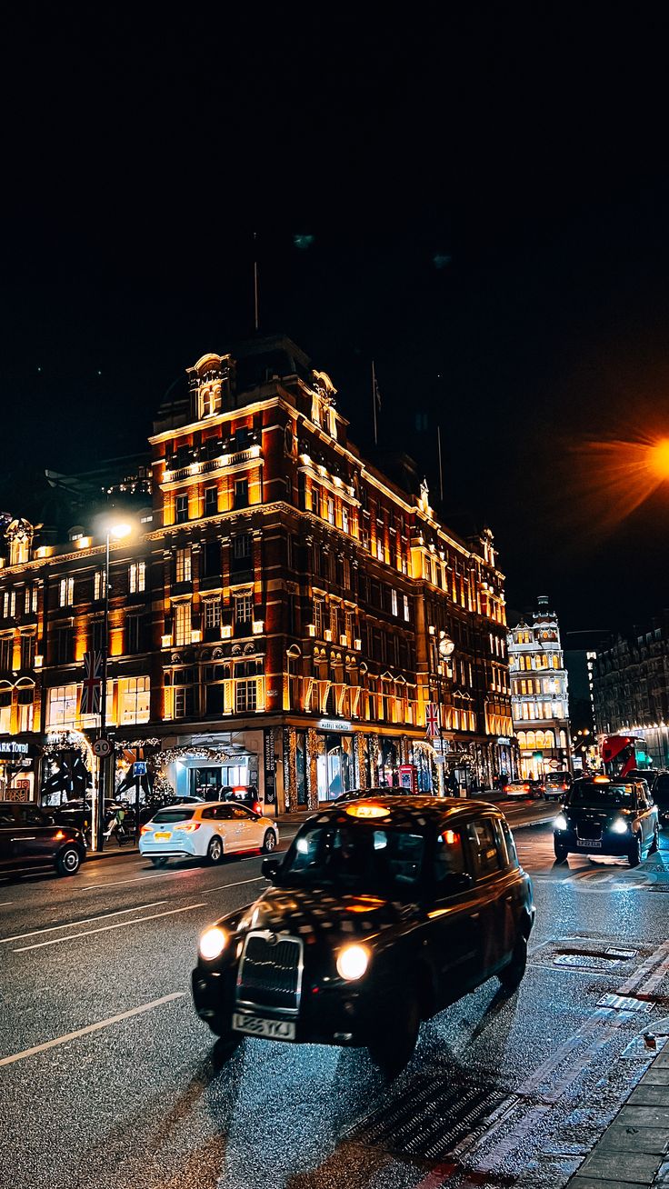 cars driving down the street at night in front of a tall building with many windows