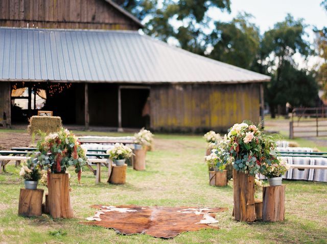 an outdoor ceremony setup with wooden stumps and flowers on the ground in front of a barn