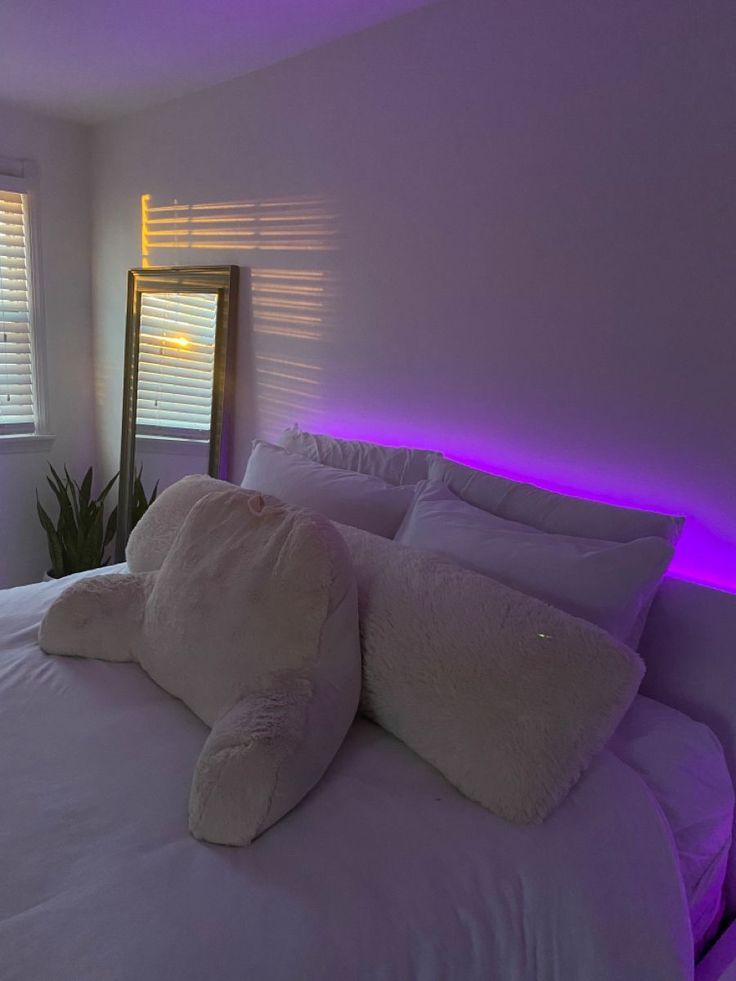 a bed with white pillows and purple lights in a room that looks like it has been turned on