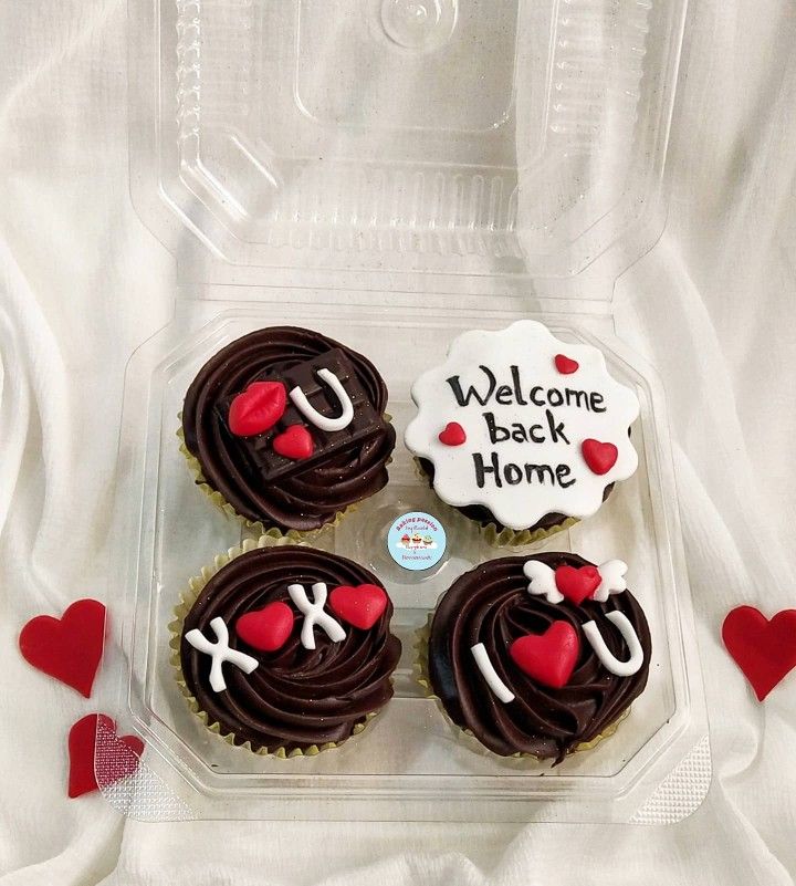 three decorated cupcakes in a plastic container with welcome back home written on them