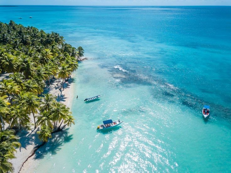 two boats are on the water near some palm trees and blue water with white sand