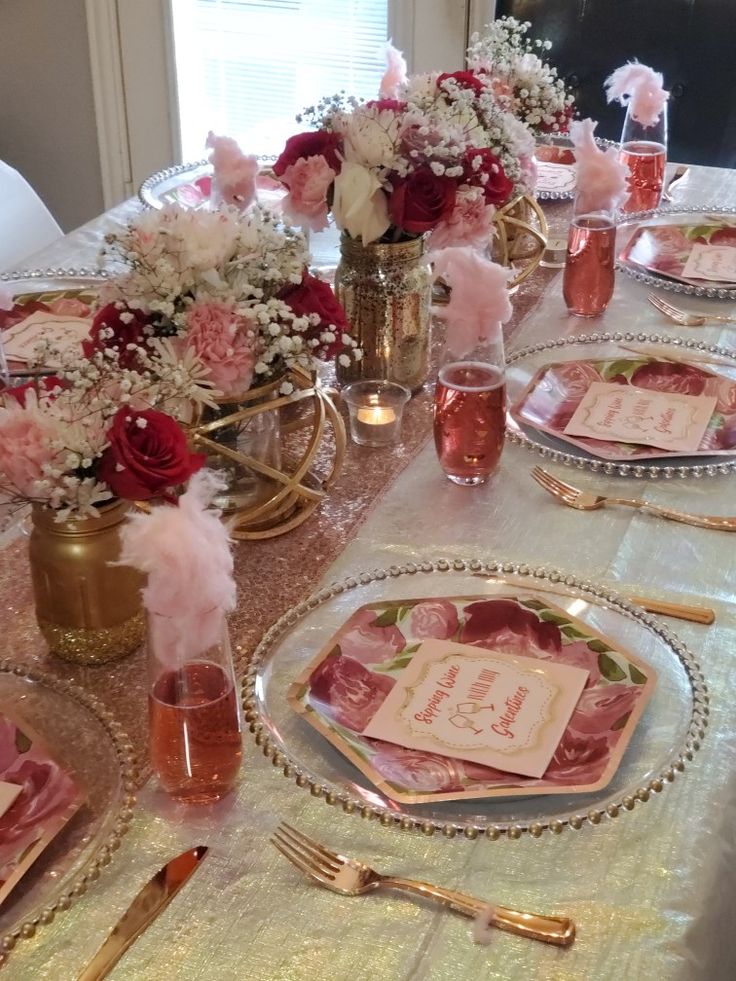 the table is set with pink and white flowers in vases, napkins, and place settings