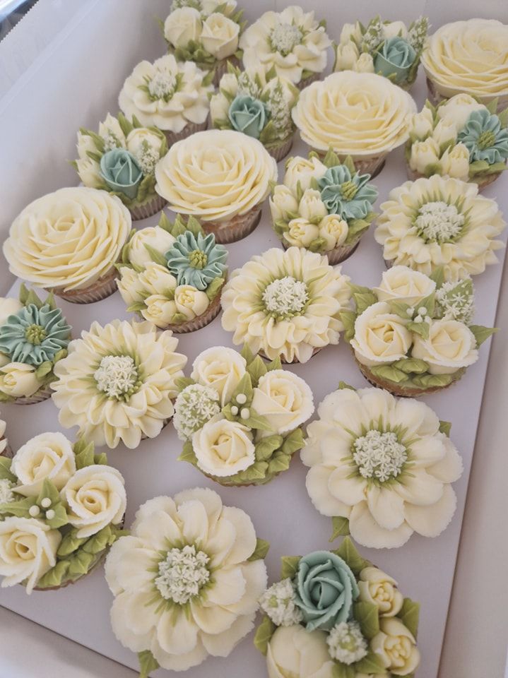 cupcakes decorated with white and green flowers in a box