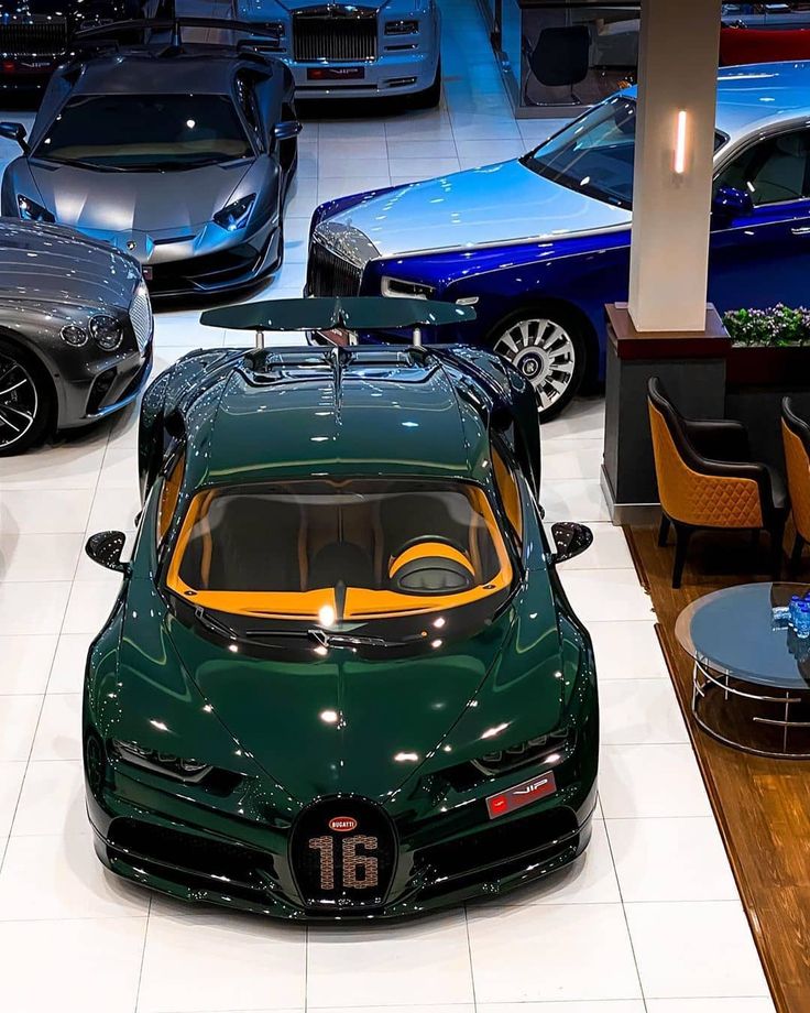 several cars are parked in a showroom, one is green and the other is blue