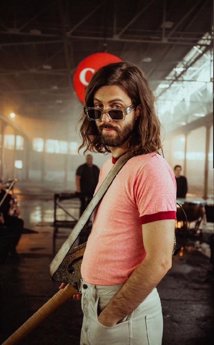 a man with long hair and glasses holding a baseball bat in an industrial building,