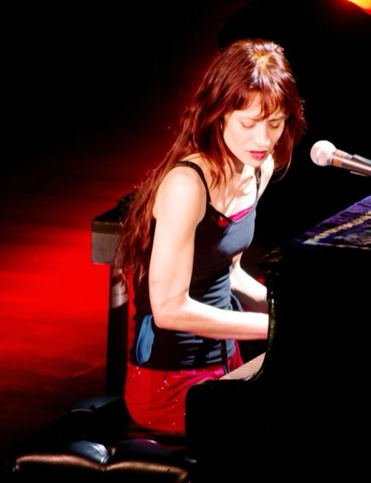 a woman sitting at a piano in front of a microphone and playing the keyboard with her hands