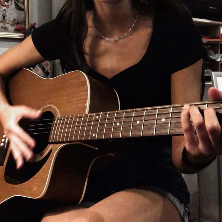 a woman sitting down playing an acoustic guitar