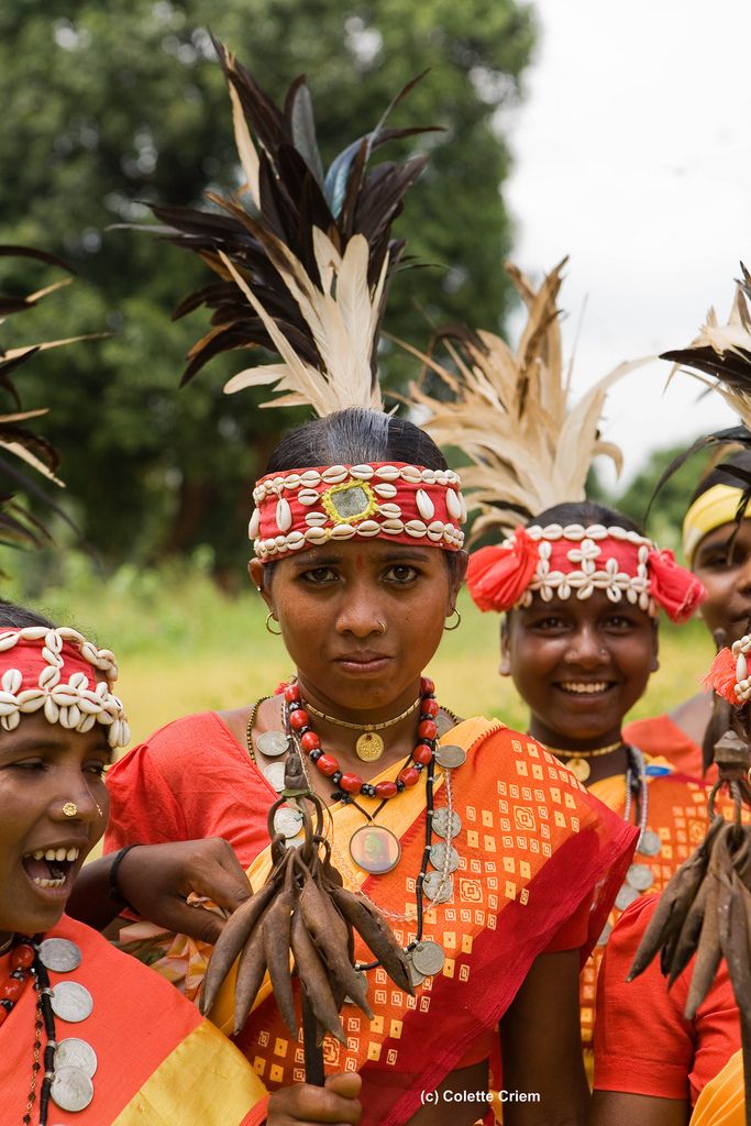 some people are wearing headdresses and smiling for the camera with trees in the background