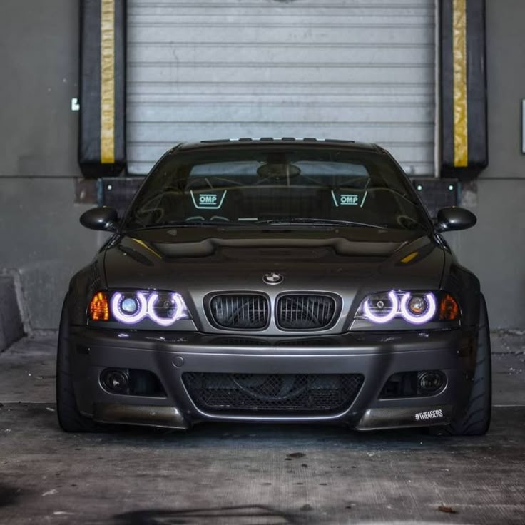 the front end of a black car with its lights turned on in a garage area