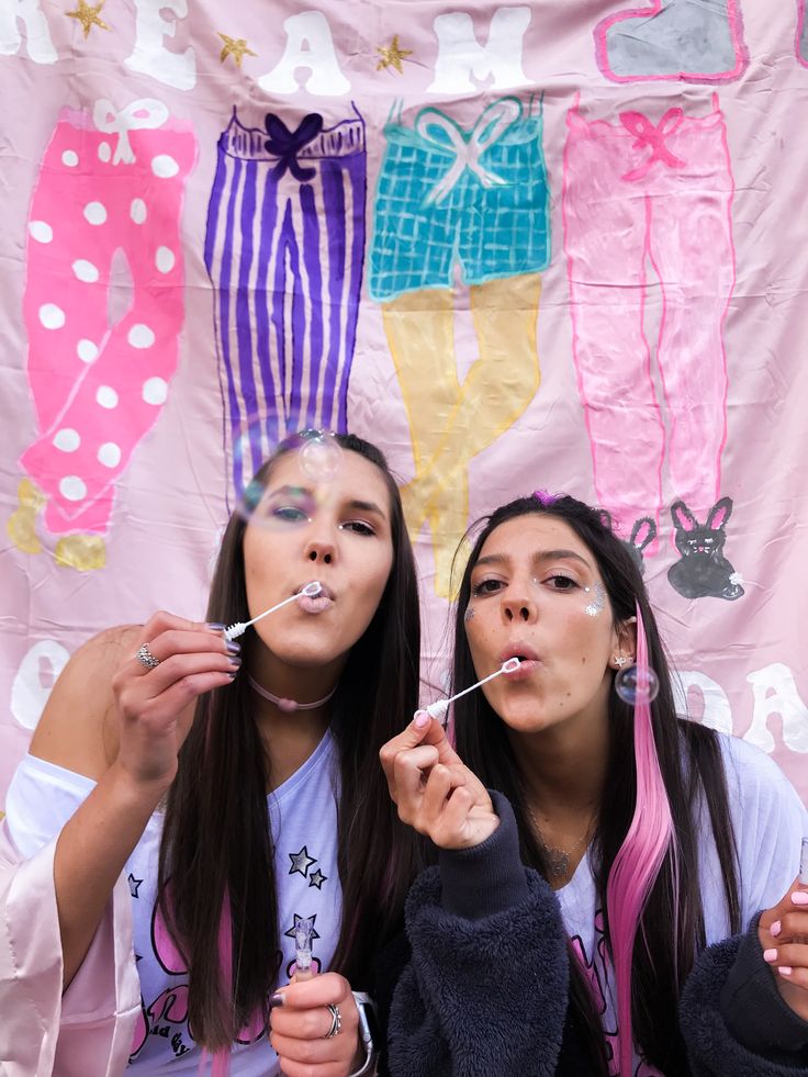 two girls blowing bubbles in front of a pink backdrop