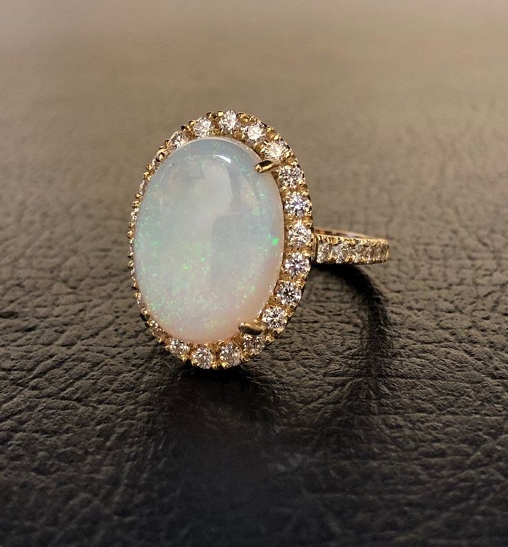 DeKara Designs Collection Our latest design! An Elegant Art Deco Inspired Australian Opal Surrounded by Beautiful Round Diamonds in an Halo 14K Yellow Gold Setting. Metal- 14K Yellow Gold, .583. The Opal is a fully cabochon cut Australian Opal. Not lab created, not a doublet, or a triplet. Stones- Center Features an Oval Fiery Australian Opal 5.80-6.00 Carats 15.60 MM Long, 11.50 MM Wide, 34 Round Diamonds, F-G Color VS1 Clarity, 0.92 Carats. The opal will be matched as close as possible to the Luxury Oval Wedding Ring, Luxury Oval Opal Ring For Anniversary, Luxury White Oval Cabochon Ring, Anniversary Opal Ring Stamped 14k In Oval Shape, Luxury Yellow Gold Opal Ring With Halo Setting, Luxury Oval White Gold Opal Ring, Oval Opal Halo Ring In 14k Gold, Exquisite Oval Opal Ring, Heirloom Opal Ring With Diamond In Oval Shape