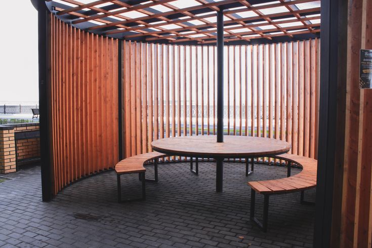 a wooden table and benches in front of an outdoor area with slatted walls