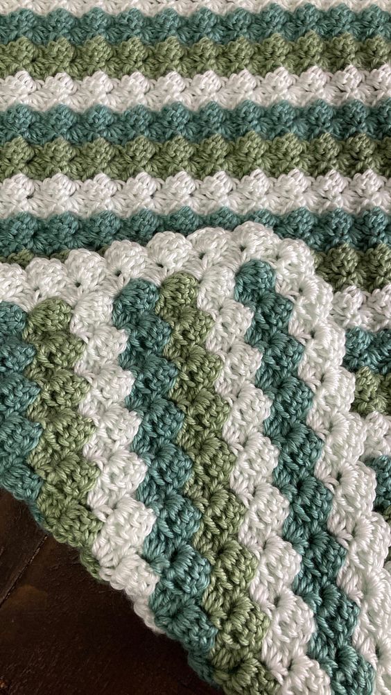 a green and white crocheted blanket sitting on top of a wooden floor