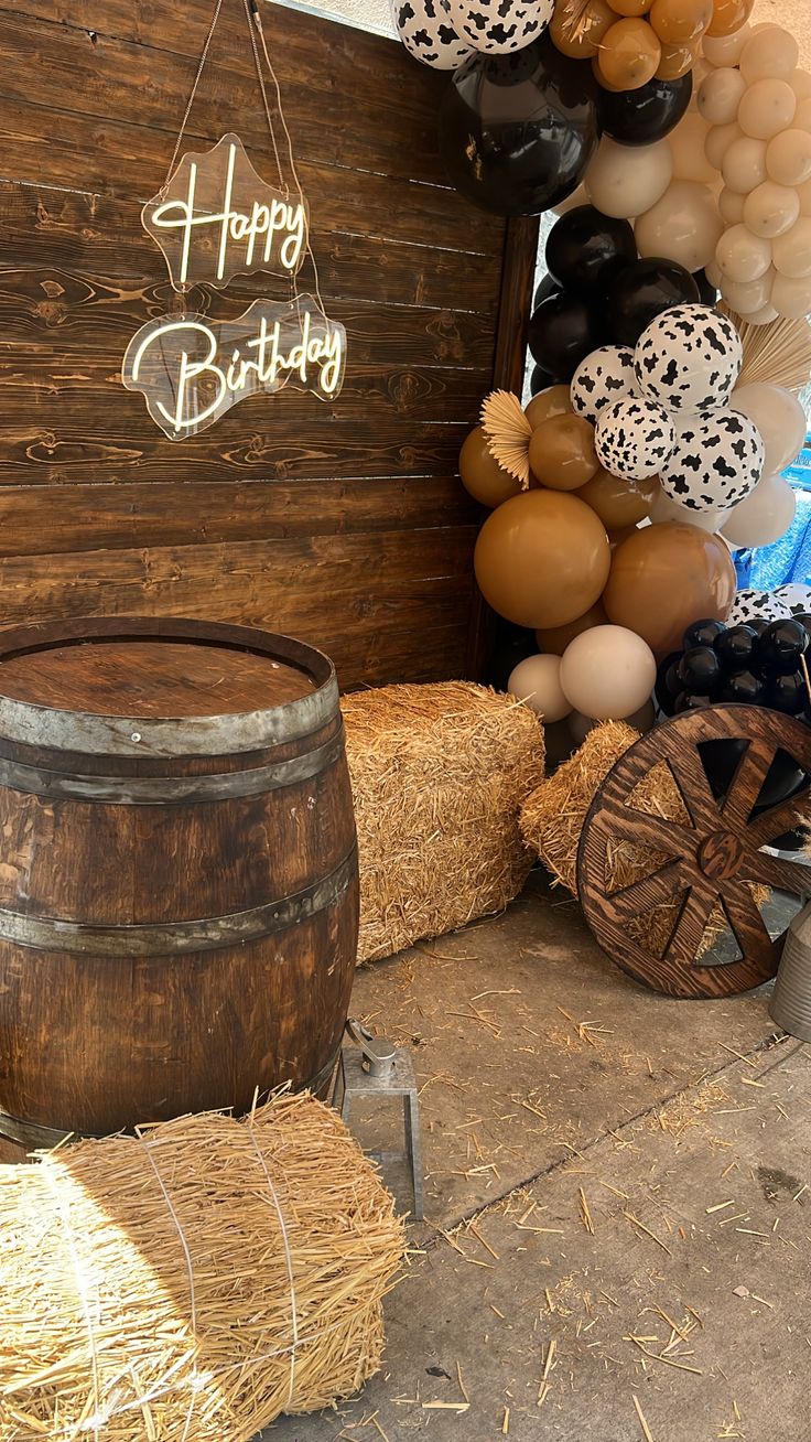 balloons and hay bales in front of a happy birthday sign on a wooden wall