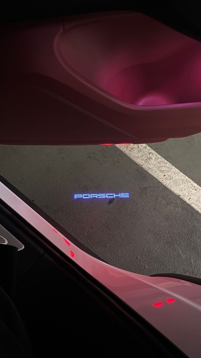 the word porsche is illuminated in red and blue on the floor next to an open car door