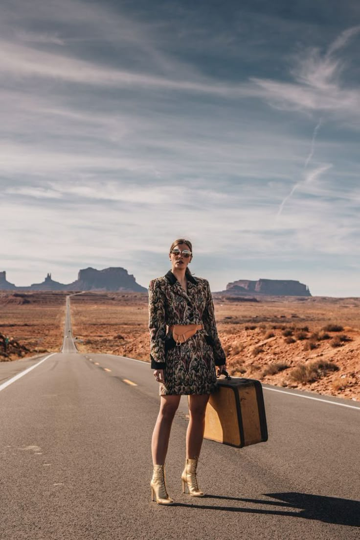 a woman standing in the middle of an empty road holding a suitcase and smiling at the camera