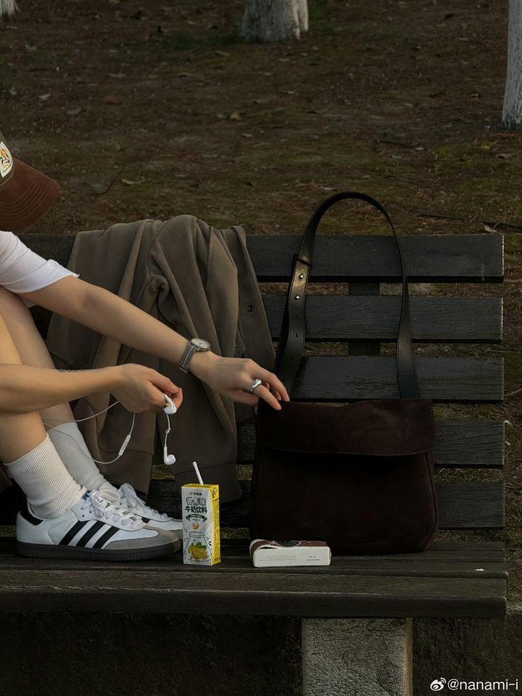 a woman is sitting on a bench with her purse and cell phone in front of her