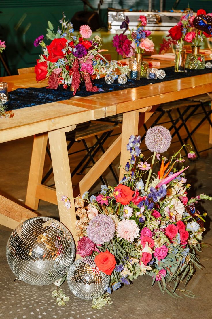 a wooden table topped with lots of different types of flowers and disco ball vases