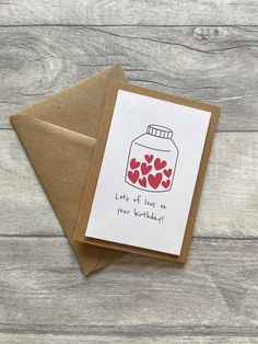 a card with hearts in a jar on top of a wooden table next to a brown envelope