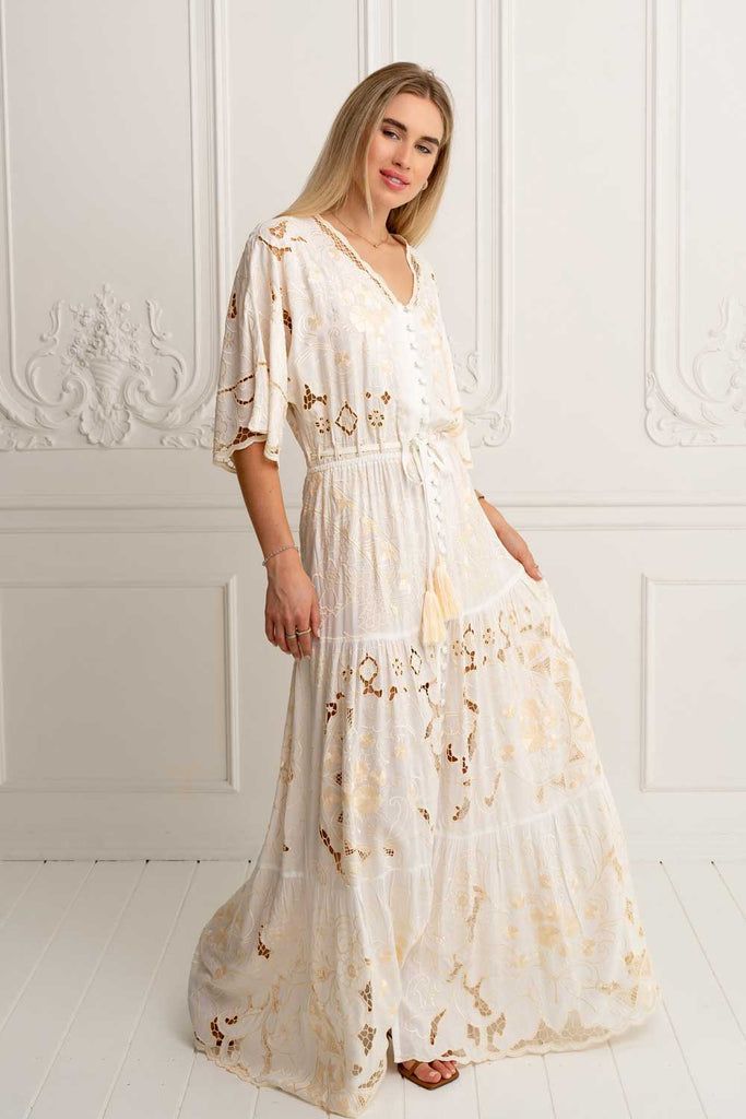 Meet the mesmerising Isla Kimono Dress in Ivory ~ a masterpiece that seamlessly weaves together sophistication and elegance, adorned with floral embroidered motifs contrasting in beige and our signature cut out work that creates delicate lace details throughout. Crafted from luxurious soft rayon our Isla Dress is captivating, a structural marvel designed to embrace your every move with grace. This beauty features an elastic drawstring waist as well as button-through bodice that can be worn open Elegant V-neck Dress With Chikankari Embroidery, Beige Lace Dress With Floral Embroidery, Feminine Long Cream Dress, Elegant Floor-length Chikankari Embroidered Dress, Elegant Maxi Embroidered Dress With Intricate Embroidery, Elegant Cream Embroidered Dress With Floral Details, Beige Embroidered Lace Dress, Elegant White Embroidered V-neck Dress, Elegant Embroidered Wedding Dress With Lace Trim