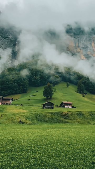 a green field with houses on it and clouds in the sky