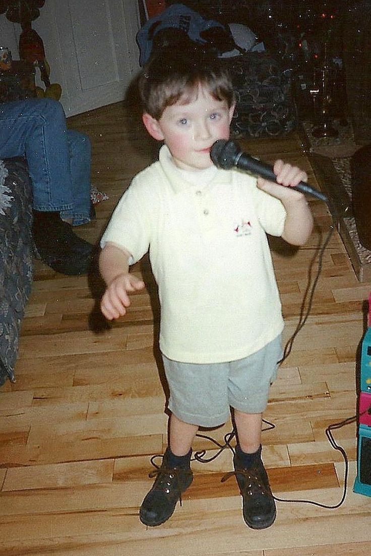 a young boy standing in front of a microphone on top of a hard wood floor