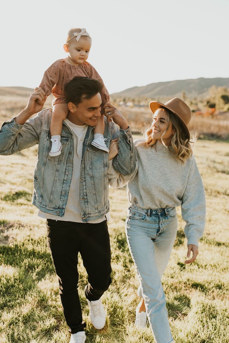 a man and woman are walking through the grass with a baby on their shoulders,