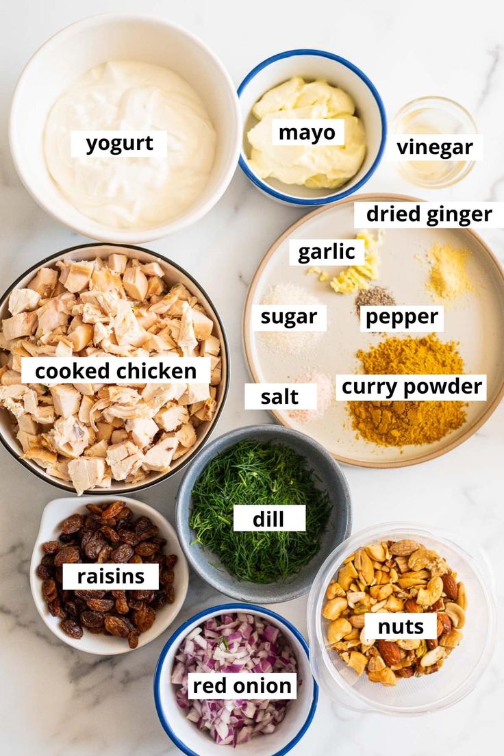 the ingredients for chicken salad laid out in bowls on a marble counter top with names