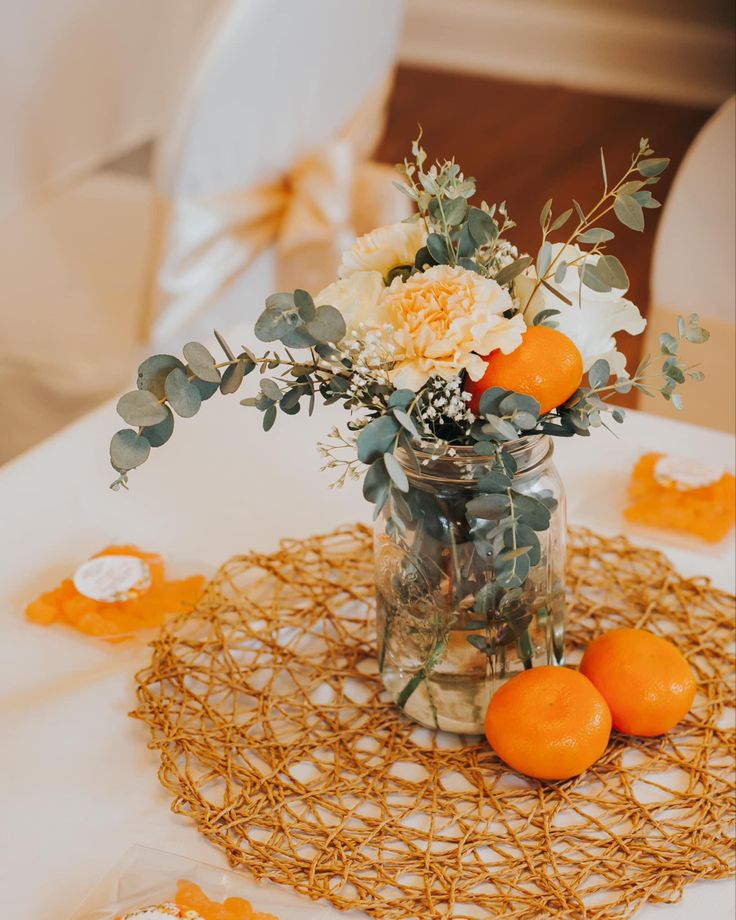 an arrangement of flowers and oranges in a mason jar on top of a table