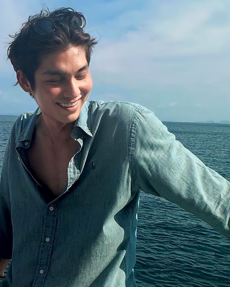 a young man standing on top of a boat near the ocean with his arms out