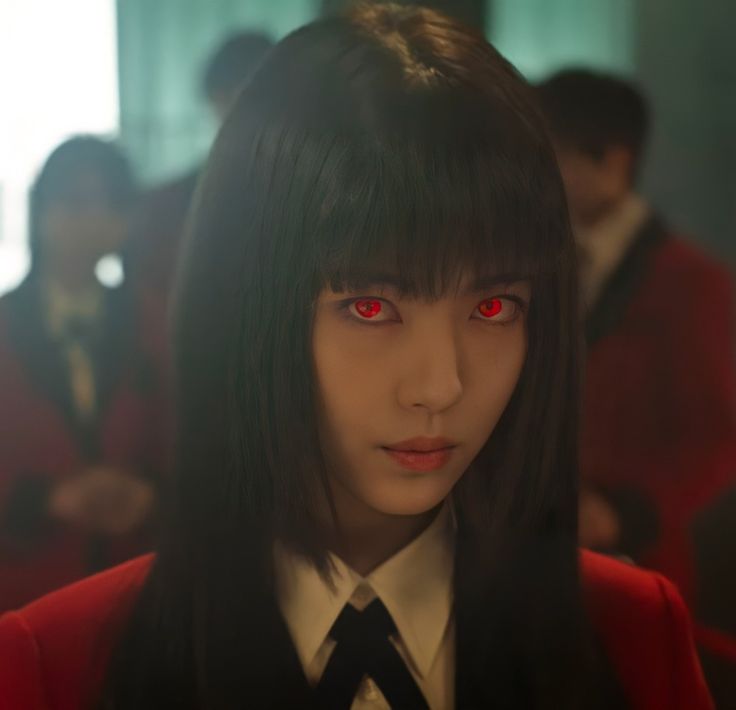 a woman with long black hair and red eyes in a room full of other people