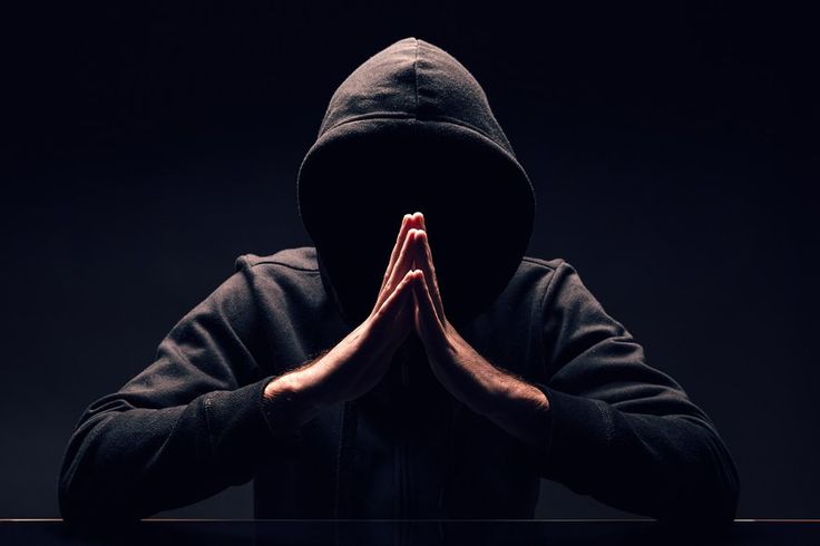 a man in a hoodie is sitting at a table with his hands folded over his face