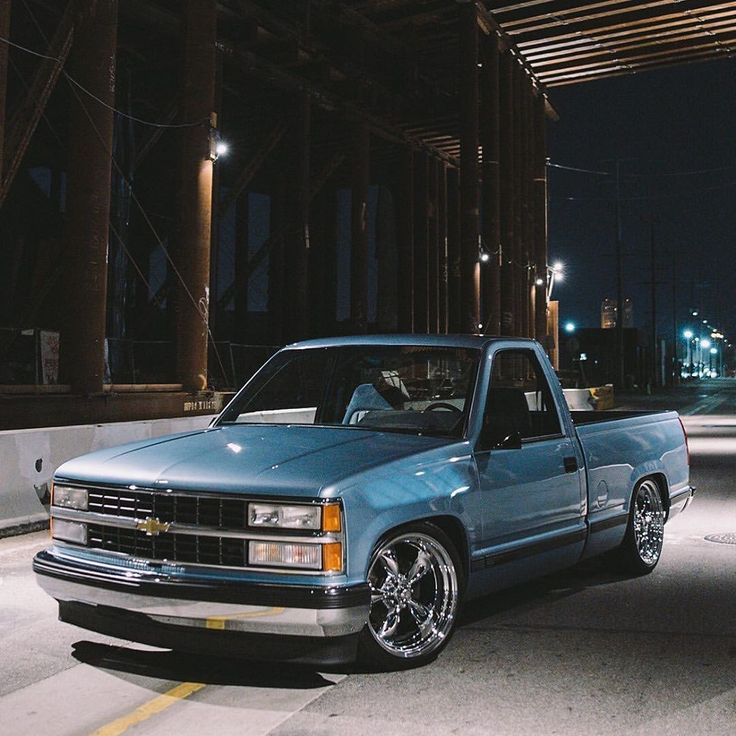 a blue pick up truck parked in an empty parking lot at night with lights on