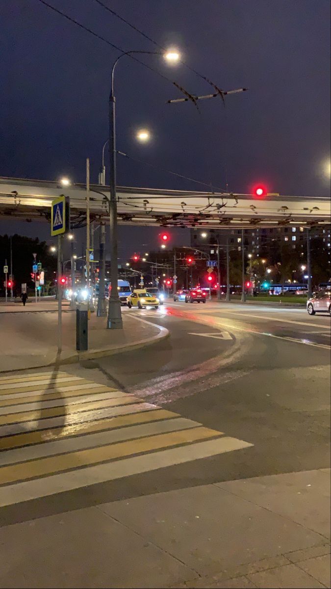 an intersection at night with cars driving on the road and traffic lights above it, all lit up