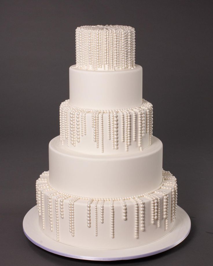 a three tiered white wedding cake with pearls on the top and sides, sitting on a plate