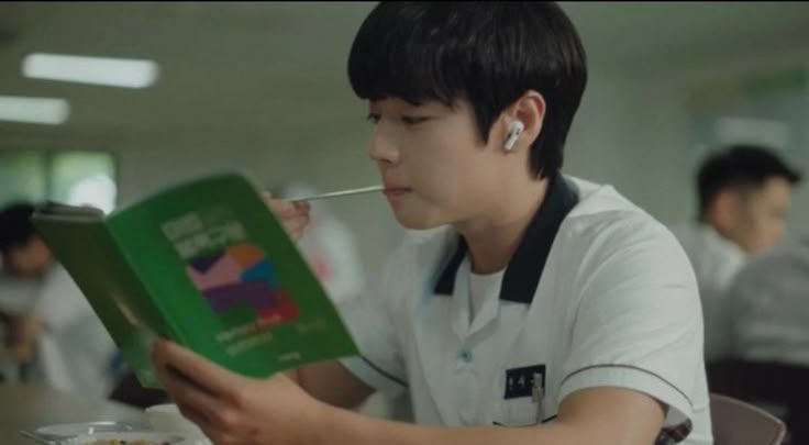 a young man sitting at a table with a book in his hand and earphones on